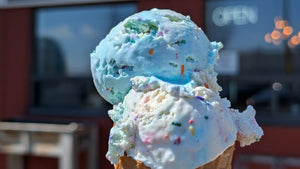 Blue ice cream cone with sprinkles held in front of a building with 'Bicycle Craft' sign.