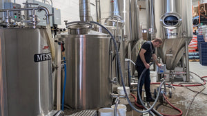 Brewery interior with large stainless steel brewing equipment and a person working.